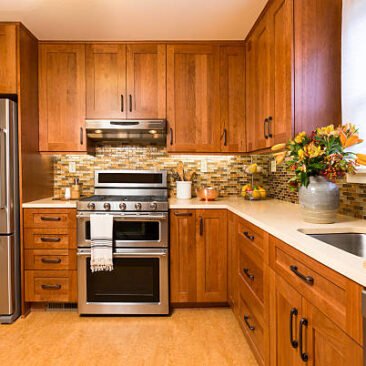 Contemporary upscale home kitchen interior with cherry wood cabinets, quartz countertops, sustainable recycled linoleum floors & stainless steel appliances including refrigerator & gas stove